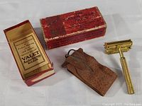 Photo of vintage gold-tone Valet Auto-Stop razor alongside worn original red box and brown leather protective case