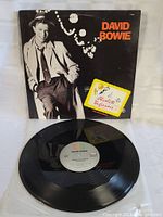 Photo of vinyl record with label showing 'David Bowie Absolute Beginners' and original cover in background.