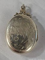Close-up of front of oval sterling silver locket showing floral carved pattern and decorative bail.