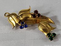 Top view of gold filled floral brooch pin with blue, red, and green jewel clusters