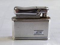 Front-facing photo of silver Colibri MCM pocket lighter with engraved 'M.W.' initials.