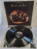 Photograph of the vinyl LP record with the record partially out of its cover, showing vinyl surface and center label with Paul McCartney Wings Band on the Run design.