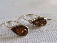 Pair of sterling silver earrings with teardrop-shaped amber stones lying on fabric background showing overall design and condition.