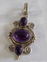 Close-up of sterling silver amethyst pendant showing the three purple cabochon stones and decorative silver scrollwork.