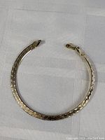 Top-down view of flat sterling silver bracelet with embossed decorative pattern and lobster claw clasp, laid out on white textured fabric.