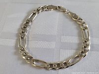 Full view of sterling silver thick link bracelet laid flat on a white textured surface showcasing the alternating oval and flat curb links and lobster claw clasp.