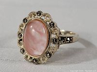 Close-up image of a sterling silver ring with a carved pink topaz center stone and dark accent stones in a floral-like design on white background.