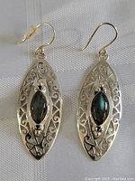 Pair of sterling silver earrings shown against white fabric background, each featuring an elongated oval filigree design with central dark marquise-shaped iridescent stones.