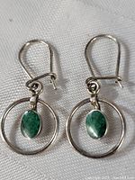 Pair of sterling silver earrings with oval malachite stone set inside circular frame, displayed on white textured fabric.