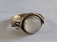 Close-up front view of sterling silver moonstone ring showing round cabochon moonstone and symmetrical scrollwork on band sides.