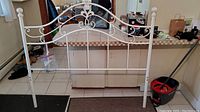 Full view of the white enameled metal queen bed headboard showing decorative scrollwork and finial posts.