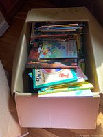 Open cardboard box filled with assorted children’s books, showing titles and colorful covers stacked inside.