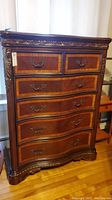 Front view showing five wooden drawers with ornate brass handles and carved decorative trim on top and bottom.