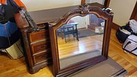 Photo of wooden-framed ornate mirror detached, positioned upright on floor.