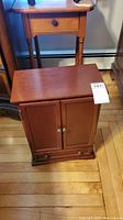 Closed wooden jewelry cabinet showing two doors and one bottom drawer