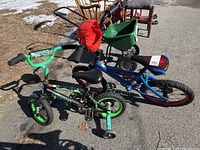 Two kids bikes side-by-side outdoors, one green with training wheels and one blue with Spiderman decorations.