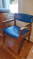 Front and side view of mid-century wooden armchair with blue vinyl upholstery, showing condition and upholstery tear.
