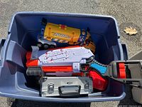 Blue plastic bin with Nerf blasters, Tonka cement mixer, smaller yellow toy truck, and silver metal case inside
