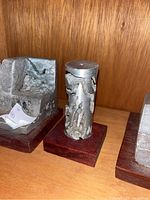 Close-up of cylinder-shaped aluminum abstract sculpture with rough surface and cut-outs mounted on wooden base.