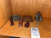 Photo showing five Buddha figurines of varying size and style on wooden shelf.