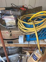 Yellow heavy-duty extension cord coiled on a shelf with painting tray, clamps in boxes, and other electrical supplies.