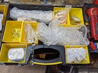 Top-view photo of the black plastic carry box containing various glass crystals, small metal hangers, and wrapped parts in yellow trays.