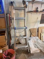 Aluminum extension ladder shown in step ladder configuration in a workshop setting with surrounding tools and supplies.