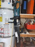 Makita electric chainsaw hanging next to a water heater and storage shelf
