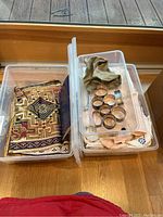 Clear plastic bin showing a folded patterned linen napkin with geometric designs and various metal napkin rings placed inside a clear bin along with some other cloth napkins.