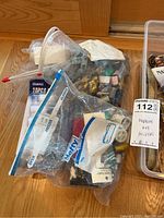 Clear plastic bags with sewing needles, thread spools and other small notions visible inside, labeled for maxsold lot 112