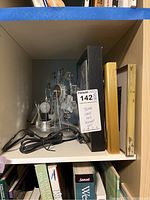 Shelf containing metal Ferris wheel solar lamp, framed artwork, and power cord.