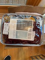 Visible sealed package of Serasoft table runners in burgundy and gold inside a box on the floor.