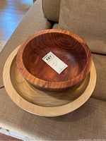 Two wooden bowls stacked on a couch, top bowl made of cherry wood with rich reddish-brown tones and bottom bowl made of lighter cedar wood.