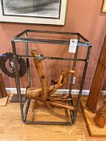 Front view of wooden sculpture inside metal frame with hardwood floor background and wall art behind.