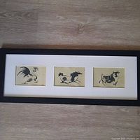 Overview of all three Chinese ink paintings of rooster, horse, and bull, framed together horizontally with white matting and dark rectangular frame on wood floor.