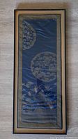 Full view of framed antique Chinese silk brocade textile. Rectangular frame with glass covering, showing dark blue silk fabric and gold embroidered roundels.