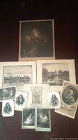 Photo shows collection of 11 antique prints laid out on dark surface, varied sizes and themes including portraits and landscapes.