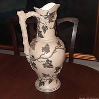 Front angle of antique cream salt glaze pottery ewer with metallic leaf and vine overlay and branch handle