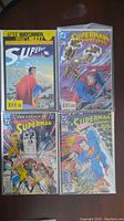 Four Superman comic books arranged in two rows, held in clear protective sleeves on a wooden surface