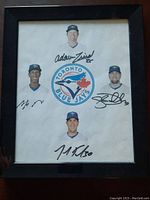 Framed photo showing heads of four Blue Jays players with signatures, frame black with minor wear.