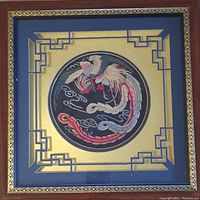 Framed embroidery piece full view showing the square frame with blue and gold geometric border and central circular embroidered phoenix.