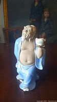Front view of the vintage Chinese Shiwan pottery mudman figure with blue robe and peach in hand, showing details of facial features and robe.