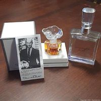 Photo showing two perfume bottles: small Oscar de la Renta bottle with ornate glass stopper on box, next to larger rectangular Moonlight Path bottle with silver-tone cap.