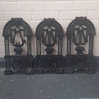 Three antique cast iron grates displayed upright against a white brick wall, showing the full set and general wear.