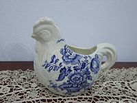 Side view of the white porcelain rooster-shaped creamer decorated with blue floral patterns.