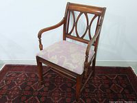Front view of antique solid wood armchair with carved wooden backrest and floral upholstered seat showing some wear and age-related distress.