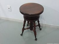 Full view of antique Victorian piano chair showing round wooden seat, adjustable height mechanism, and four legs with ball and claw feet.