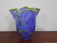 Front view of periwinkle blue hand-blown glass vase with yellow ribbon edge and green spots.