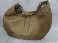 Front view of Cole Haan goldtone leather hobo bag showing leather texture, front zipper pull, and logo plaque.