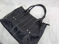 Front and part side view of the black genuine leather handbag showing handle and stitching details.